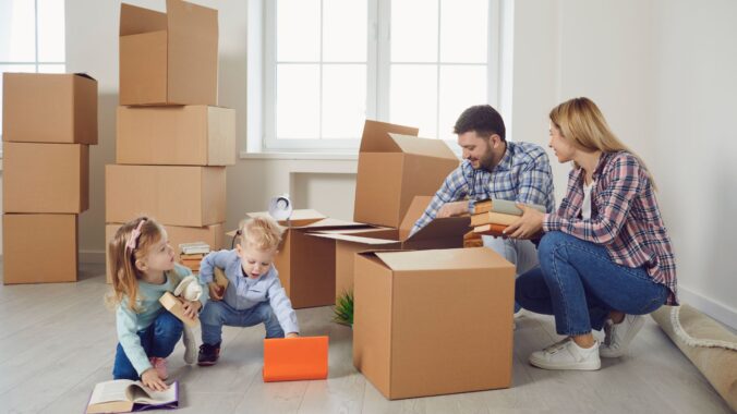 A young family with two children is unpacking cardboard boxes in their new home, surrounded by stacked moving boxes and household items capturing the stress-free relocation experience provided by movers in Newark NJ.